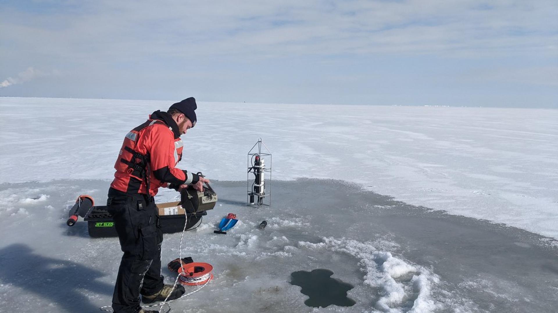 A researcher grabbing a water sample from Lake Erie during the winter.