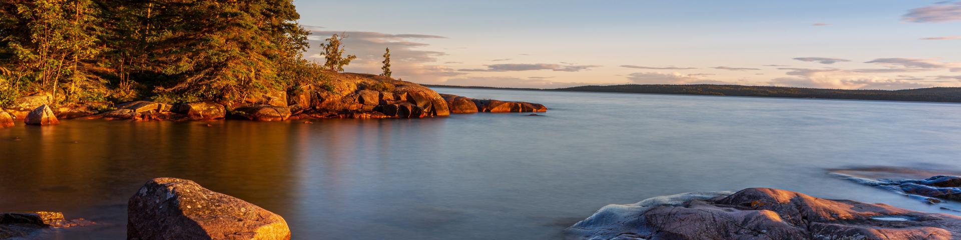 Shoreline of Lake Superior at Rossport, Ontario with pine trees and rocks at sunset